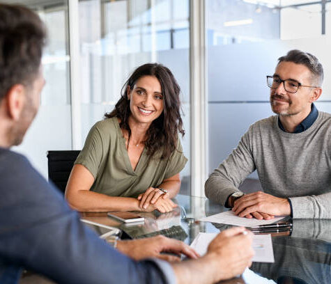 Smiling mature couple meeting with bank manager for investment. Beautiful mid adult woman with husband listening to businessman during meeting in conference room in modern office. Happy middle aged couple meeting loan advisor to buy a new home.